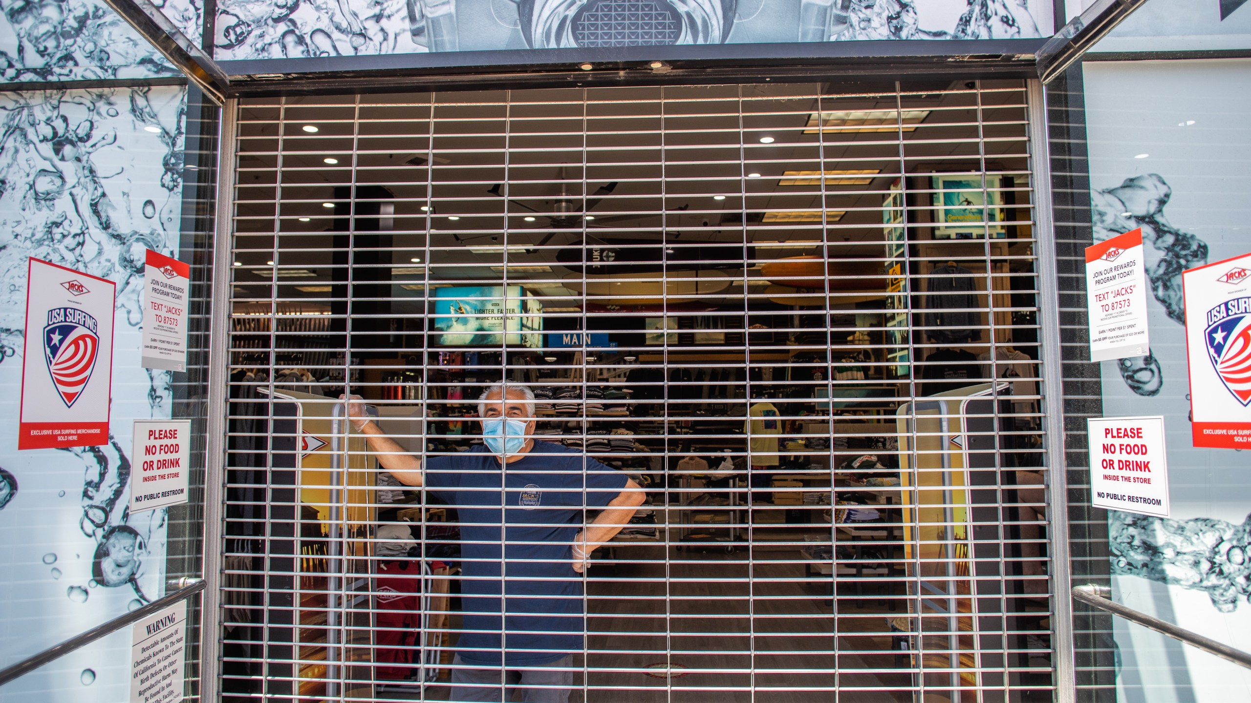 A seller inside a closed shop watches people gathering in a demonstration on May 1, 2020, in Huntington Beach, California. (Apu Gomes/Getty Images)