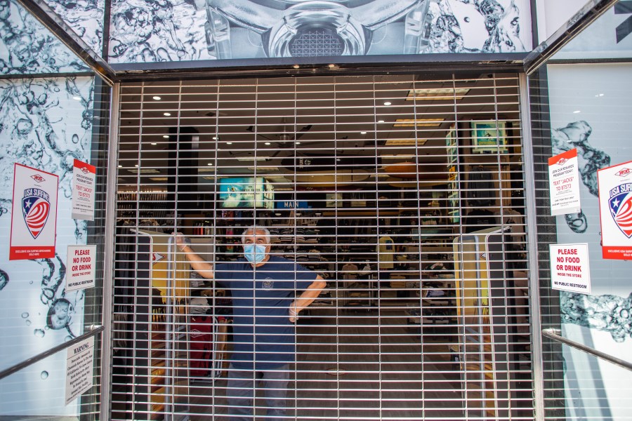 A seller inside a closed shop watches people gathering in a demonstration on May 1, 2020, in Huntington Beach, California. (Apu Gomes/Getty Images)