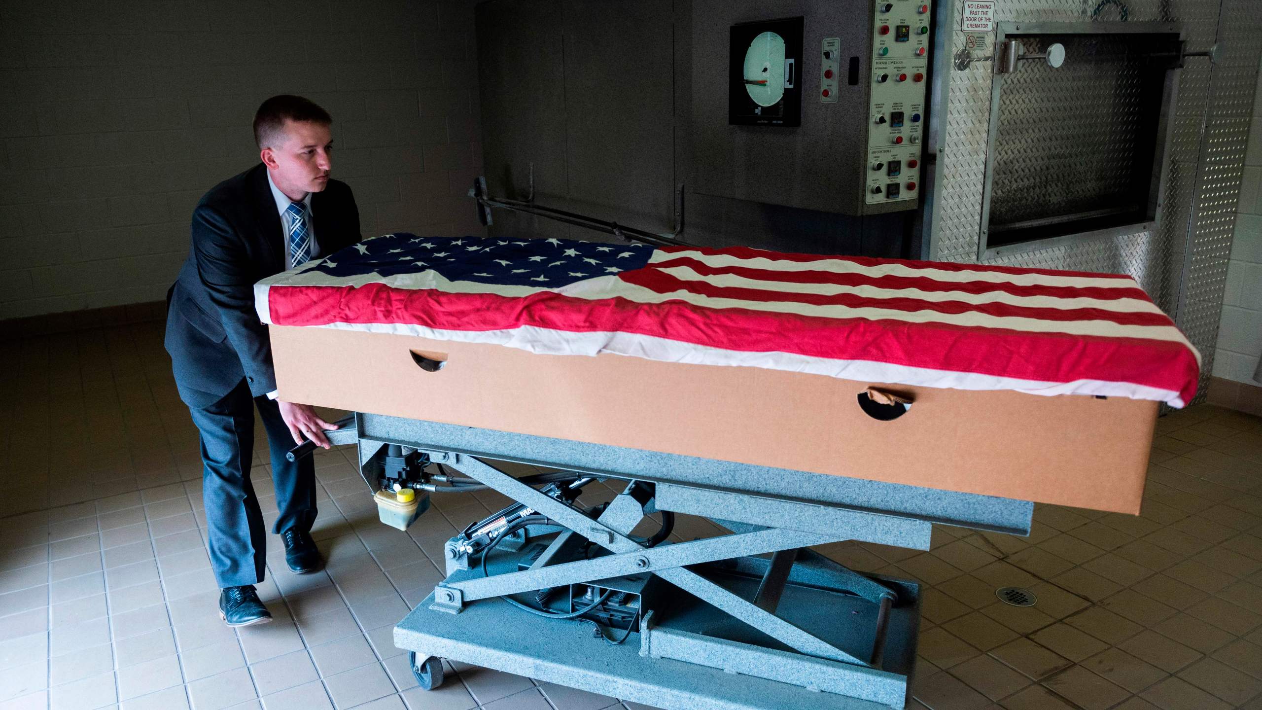 Crematory operator Brandon Cochran pushes a cremation box draped in a U.S. national flag, containing the body a veteran who died of COVID-19, to an incinerator at the Stauffer Funeral Homes in Frederick, Maryland on May 1, 2020. (ANDREW CABALLERO-REYNOLDS/AFP via Getty Images)