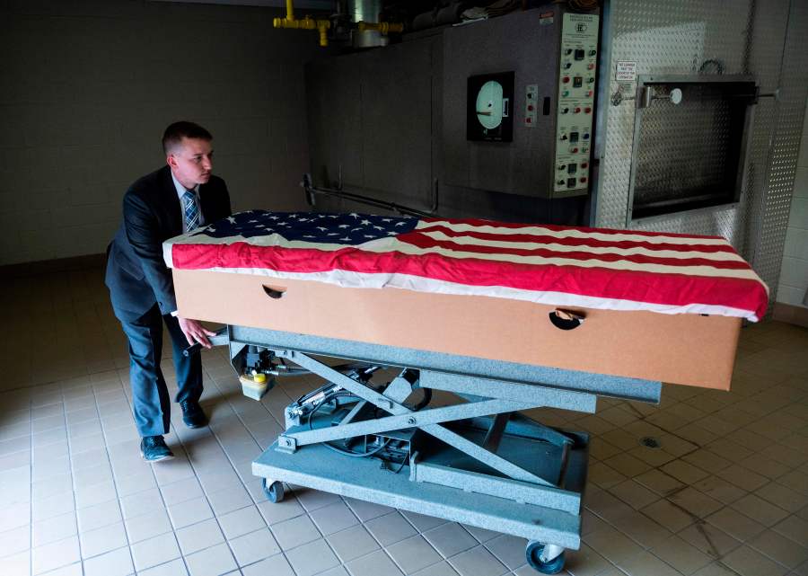 Crematory operator Brandon Cochran pushes a cremation box draped in a U.S. national flag, containing the body a veteran who died of COVID-19, to an incinerator at the Stauffer Funeral Homes in Frederick, Maryland on May 1, 2020. (ANDREW CABALLERO-REYNOLDS/AFP via Getty Images)