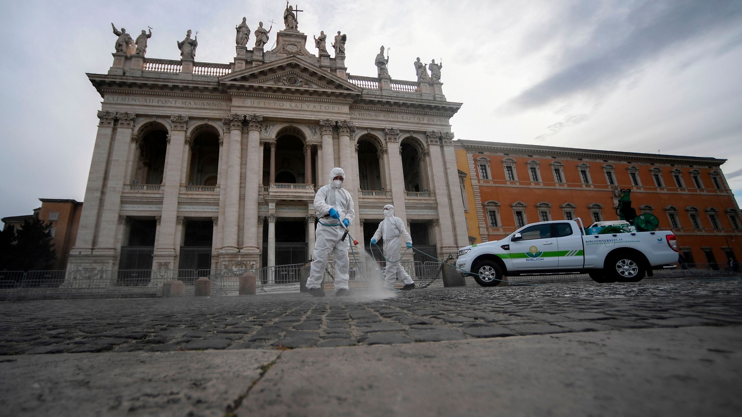 Employees of a disinfecting services company, wearing protective overalls and mask, spray sanitizer at the Archbasilica of Saint John Lateran (San Giovanni in Laterano) in Rome on May 15, 2020. (FILIPPO MONTEFORTE/AFP via Getty Images)