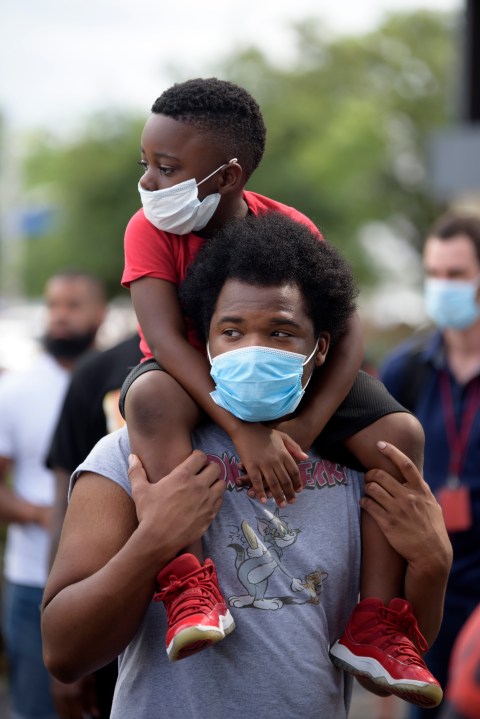 A young boy sits on the shoulder's of a man, both wearing facemasks, during a "Justice for George Floyd" event in Houston, Texas on May 30, 2020, after George Floyd, an unarmed black, died while being arrested and pinned to the ground by a Minneapolis police officer. (MARK FELIX/AFP via Getty Images)