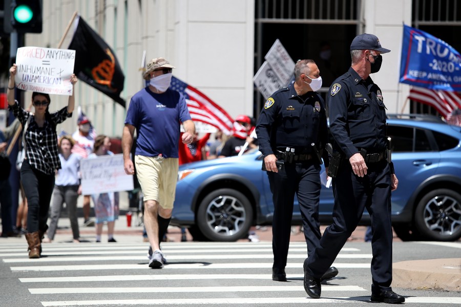 San Diego Police Department officers look on as activists hold signs and protest the California lockdown due to the coronavirus pandemic on May 1, 2020, in San Diego. (Sean M. Haffey/Getty Images)