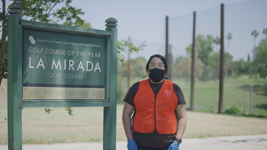 A park monitor for Los Angeles County Parks and Recreation stands beside the sign for La Mirada Golf Course in a photo provided by the agency on May 10, 2020.