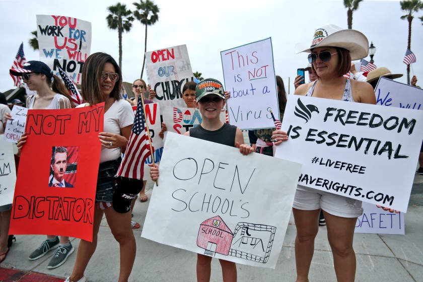 A young demonstrator holds a sign asking for schools to be reopened during a protest at Pier Plaza in Huntington Beach on May 9.(Raul Roa / Los Angeles Times)