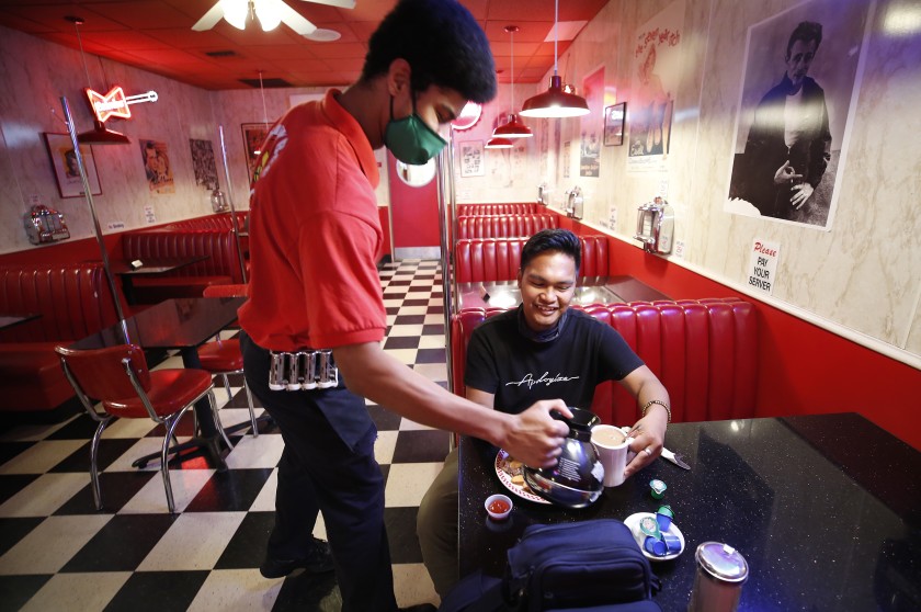 At the Busy Bee Cafe along Main Street in downtown Ventura, Bryson Finger serves coffee to Jeric Gambon, 24, as he enjoys breakfast May 21, 2020.(Al Seib / Los Angeles Times)