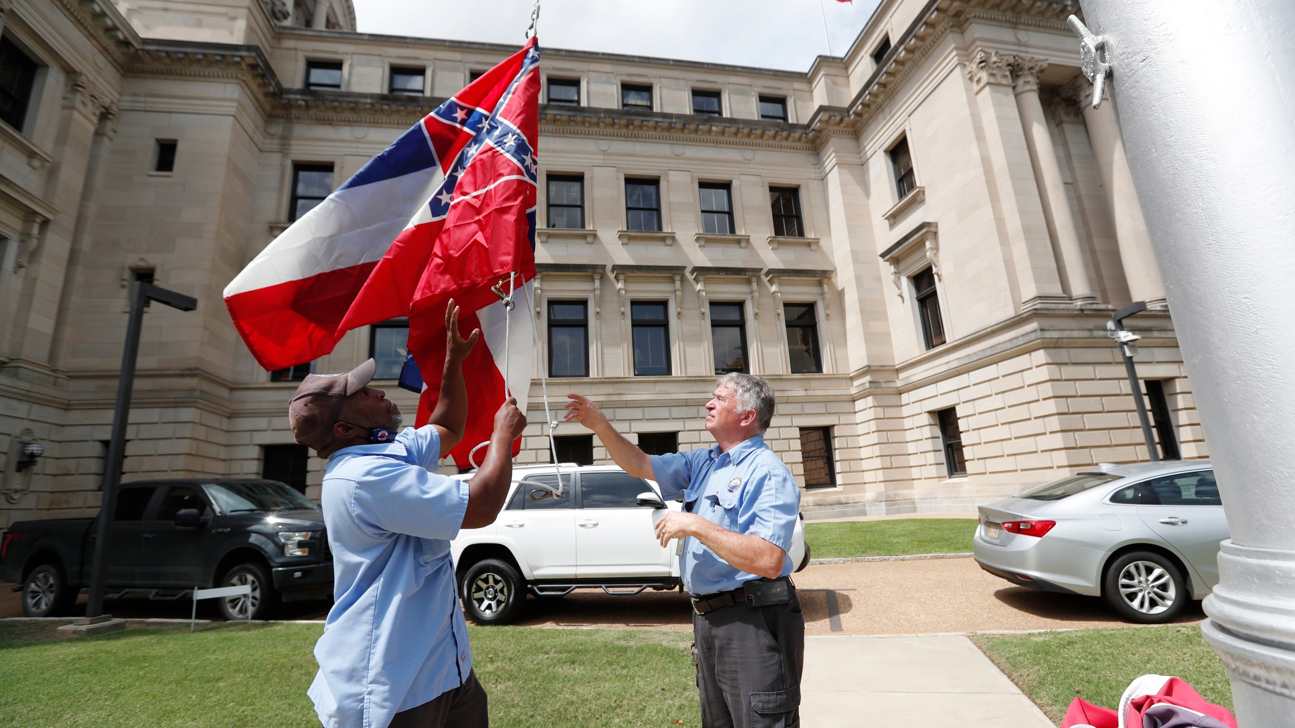 Mississippi Department of Finance and Administration employees Willie Townsend, left, and Joe Brown, raise a couple of Mississippi state flags over the Capitol grounds in Jackson on June 30, 2020. (Rogelio V. Solis/Associated Press)