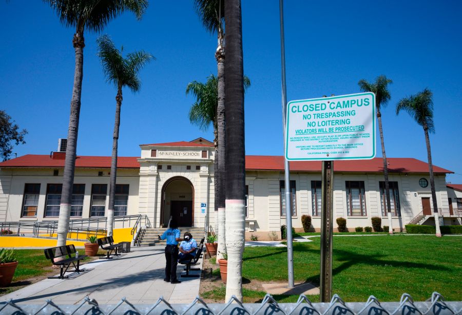 Two security guards talk on the campus of the closed McKinley School, part of the Los Angeles Unified School District system, in Compton on April 28, 2020. (ROBYN BECK/AFP via Getty Images)