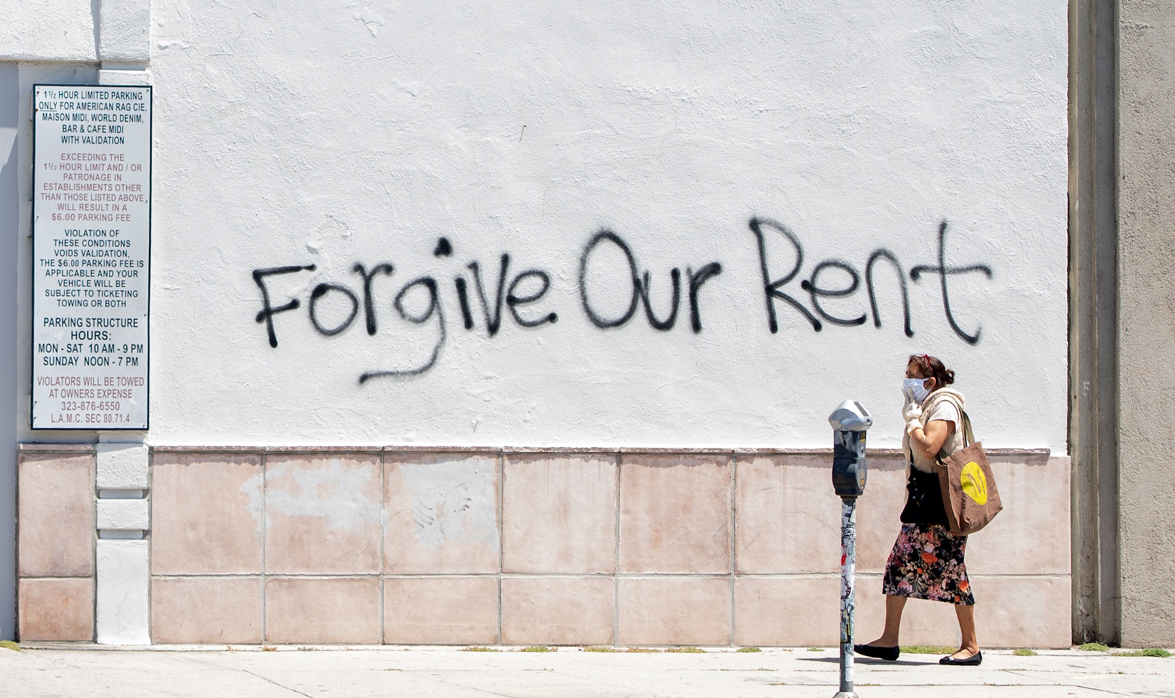 A woman wearing a mask walks past a wall bearing a graffiti asking for rent forgiveness on La Brea Ave amid the COVID-19 pandemic on May 1, 2020. (Valeria Macon /AFP / Getty Images)