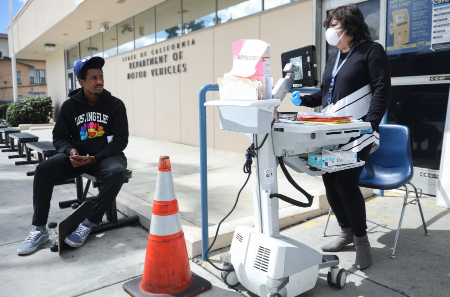 A Department of Motor Vehicles worker speaks with a man who did not have an appointment at an appointment desk in front of the DMV building, with a cone used to implement social distancing, on March 23, 2020 in Los Angeles. (Mario Tama/Getty Images)