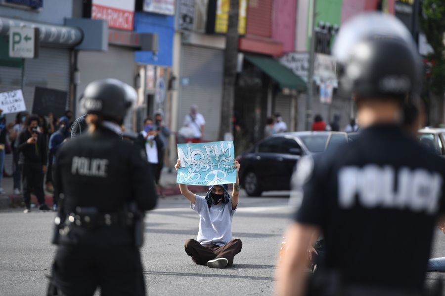 A demonstrator holds a sign as he sits in front of police in Van Nuys on June 1, 2020. (Robyn Beck / AFP / Getty Images)