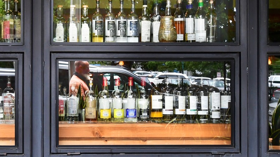 A pedestrian's reflection is seen while walking past bottles of liquor at a bar in Los Angeles on June 29, 2020. (Frederic J. Brown / AFP / Getty Images)