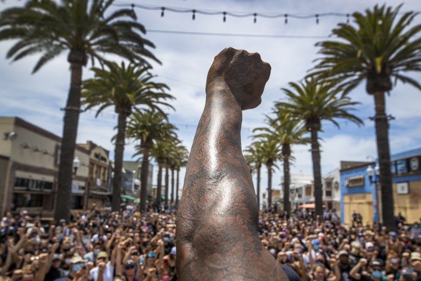 Black Lives Matter protesters take a knee and raise their fists during a moment of silence to honor George Floyd at the Hermosa Beach Pier in June 2020. (Allen J. Schaben / Los Angeles Times)