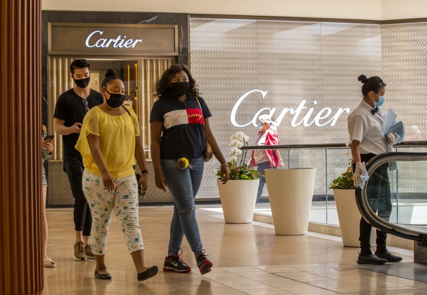 Glenby Ramirez, right, wipes down the escalator handrail as shoppers pass by at South Coast Plaza in Costa Mesa on June 11, 2020. (Allen J. Schaben / Los Angeles Times)