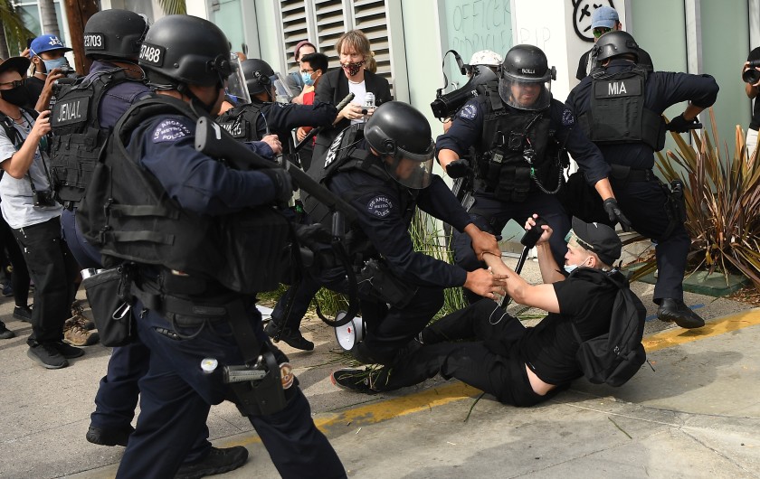 An LAPD officer holds a less-lethal launcher as fellow officers take a protester into custody during a demonstration in the Fairfax District in June 2020. (Wally Skalij / Los Angeles Times)