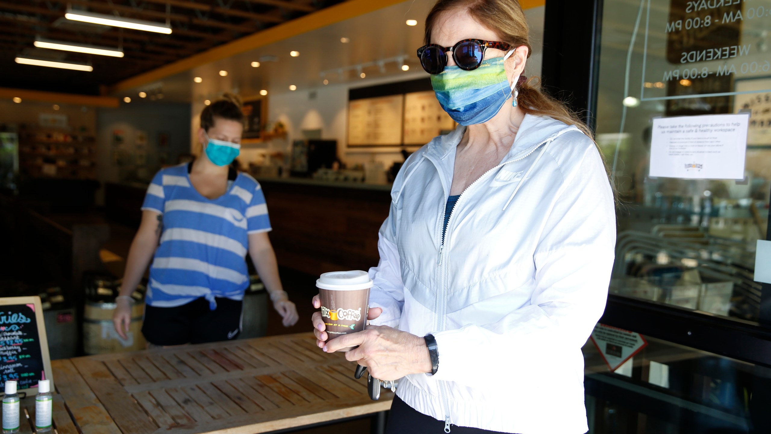 Barbara Meier, right, wears a face mask as picks up her drink order from Philz Coffee in Davis on April 27, 2020. (Rich Pedroncelli/Associated Press)