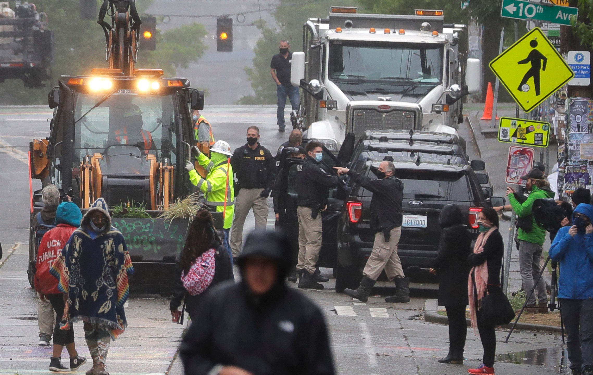 Seattle Police, at right, look on as Department of Transportation workers remove barricades at the intersection of 10th Ave. and Pine St., Tuesday, June 30, 2020 at the CHOP (Capitol Hill Occupied Protest) zone in Seattle. (AP Photo/Ted S. Warren)