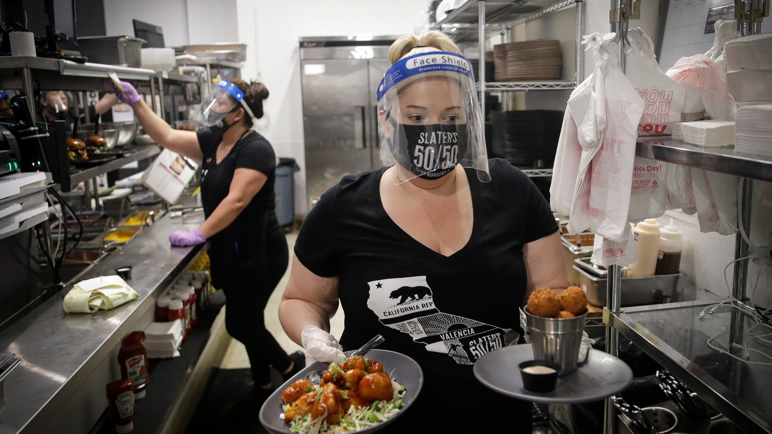 A waitress takes a food order from the kitchen at Slater's 50/50 on July 1, 2020, in Santa Clarita. (AP Photo/Marcio Jose Sanchez)