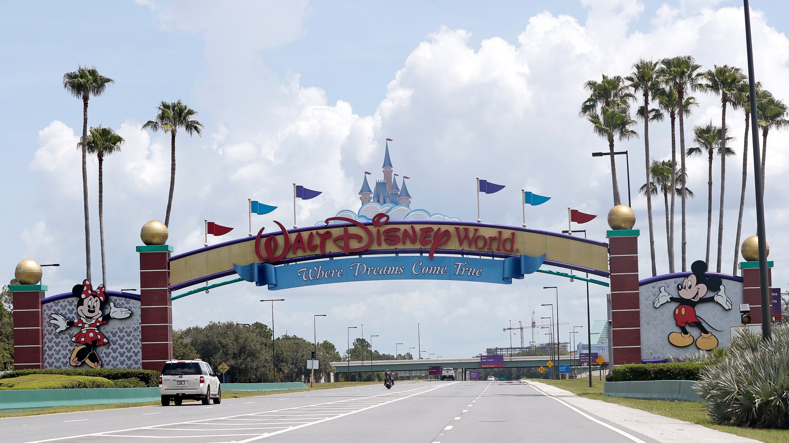 Cars drive under a sign greeting visitors near the entrance to Walt Disney World, in Lake Buena Vista, Florida on July 2, 2020. (AP Photo/John Raoux, File)