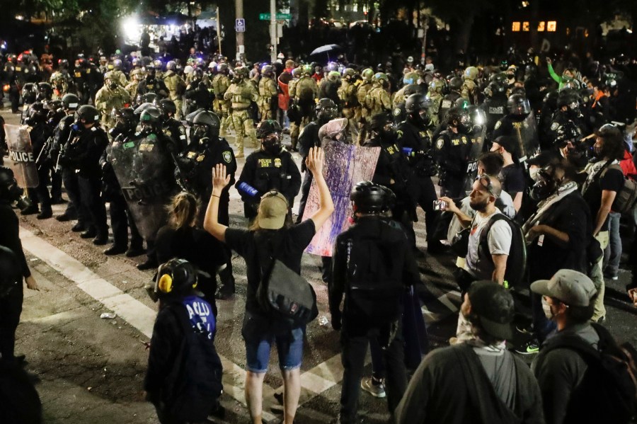 Federal police officers huddle in front of a crowd of demonstrators during a Black Lives Matter protest Sunday, July 26, 2020, in Portland, Ore. (AP Photo/Marcio Jose Sanchez)