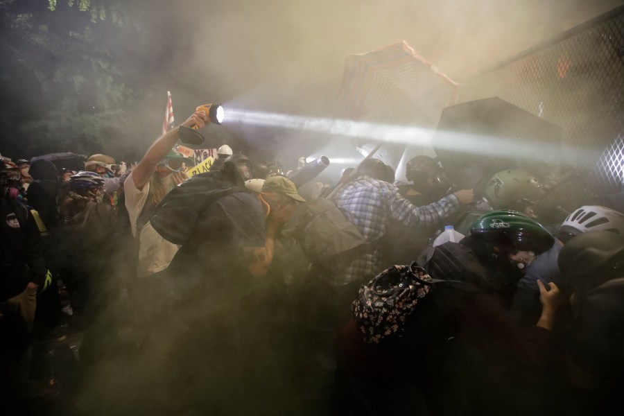 Demonstrators push on a fence as tear gas is deployed during a Black Lives Matter protest at the Mark O. Hatfield United States Courthouse Saturday, July 25, 2020, in Portland, Ore. (AP Photo/Marcio Jose Sanchez)