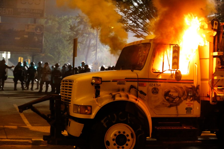 Police stand in front of a utility vehicle that was set on fire by protesters during a demonstration outside the Richmond Police Department headquarters on Grace Street in Richmond, Va., Saturday, July 25, 2020.  Police deployed flash-bangs and pepper spray to disperse the crowd after the city utility vehicle was set on fire. (Joe Mahoney/Richmond Times-Dispatch via AP)