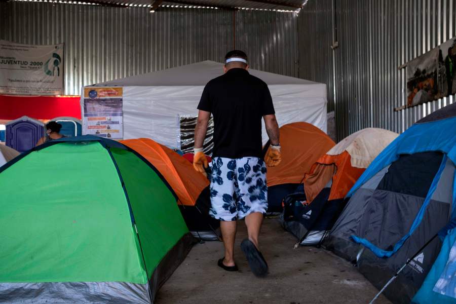 An asylum seeker walks among tents, with one in the background dedicated to people suspected to be infected with COVID-19, at the Juventud 2000 migrant shelter in Tijuana on June 19, 2020. (Guillermo Arias / AFP / Getty Images)