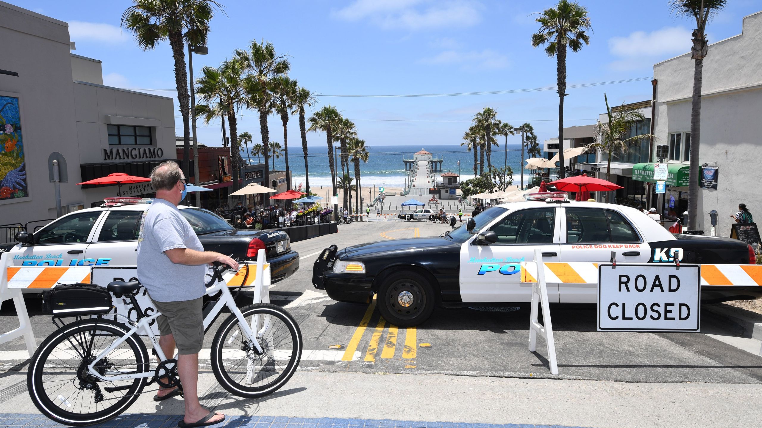 A man wearing a mask looks out over a road closed to car traffic near the pier in Manhattan Beach on July 4, 2020. (ROBYN BECK/AFP via Getty Images)