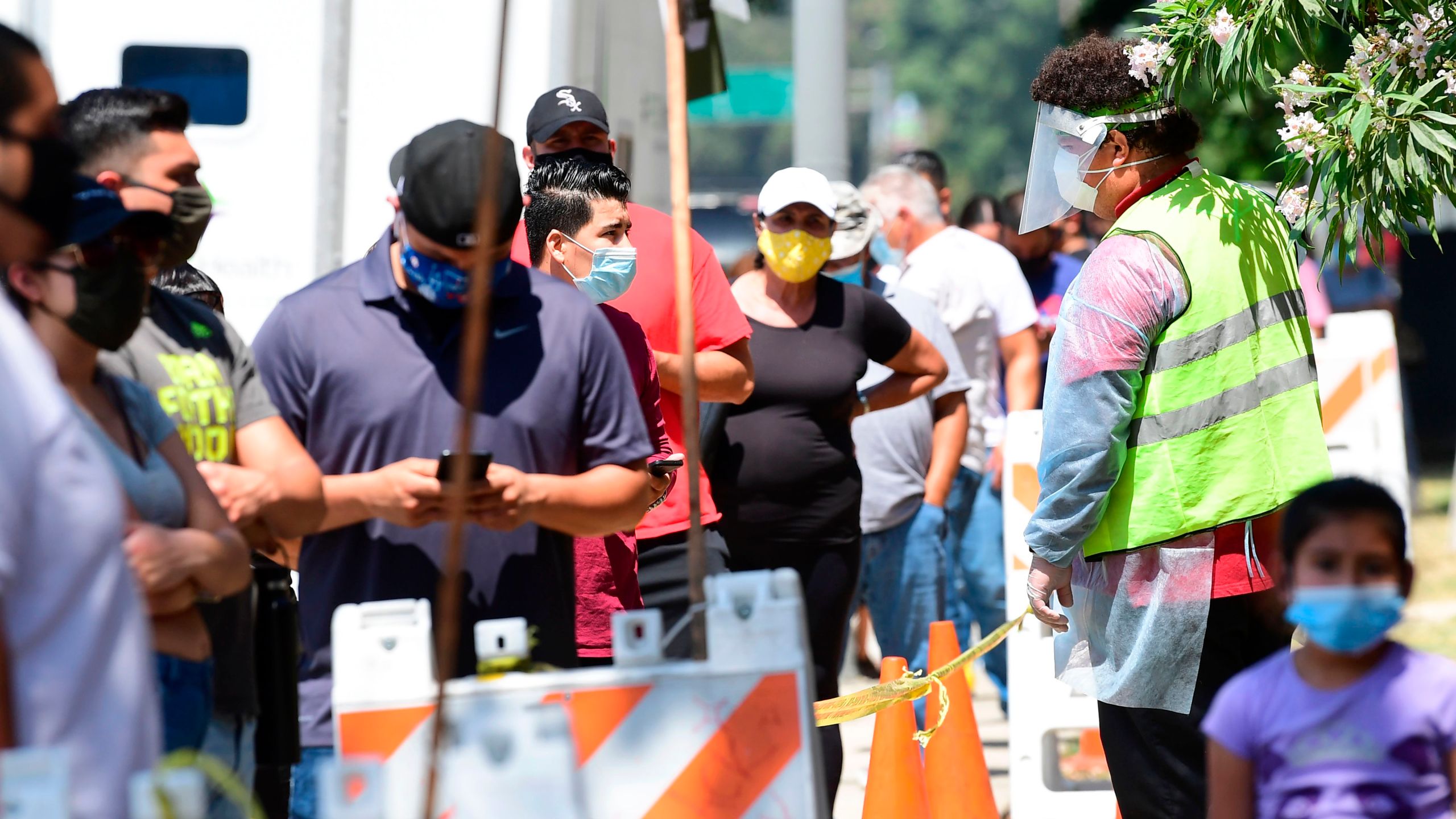 A volunteer wearing personal protective equipment speaks with people waiting in line at a walk-in coronavirus test site in Los Angeles on July 10, 2020. (Frederic J. Brown / AFP / Getty Images)