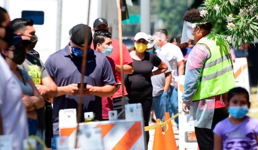 A volunteer wearing personal protective equipment speaks with people waiting in line at a walk-in coronavirus test site in Los Angeles on July 10, 2020. (Frederic J. Brown / AFP / Getty Images)