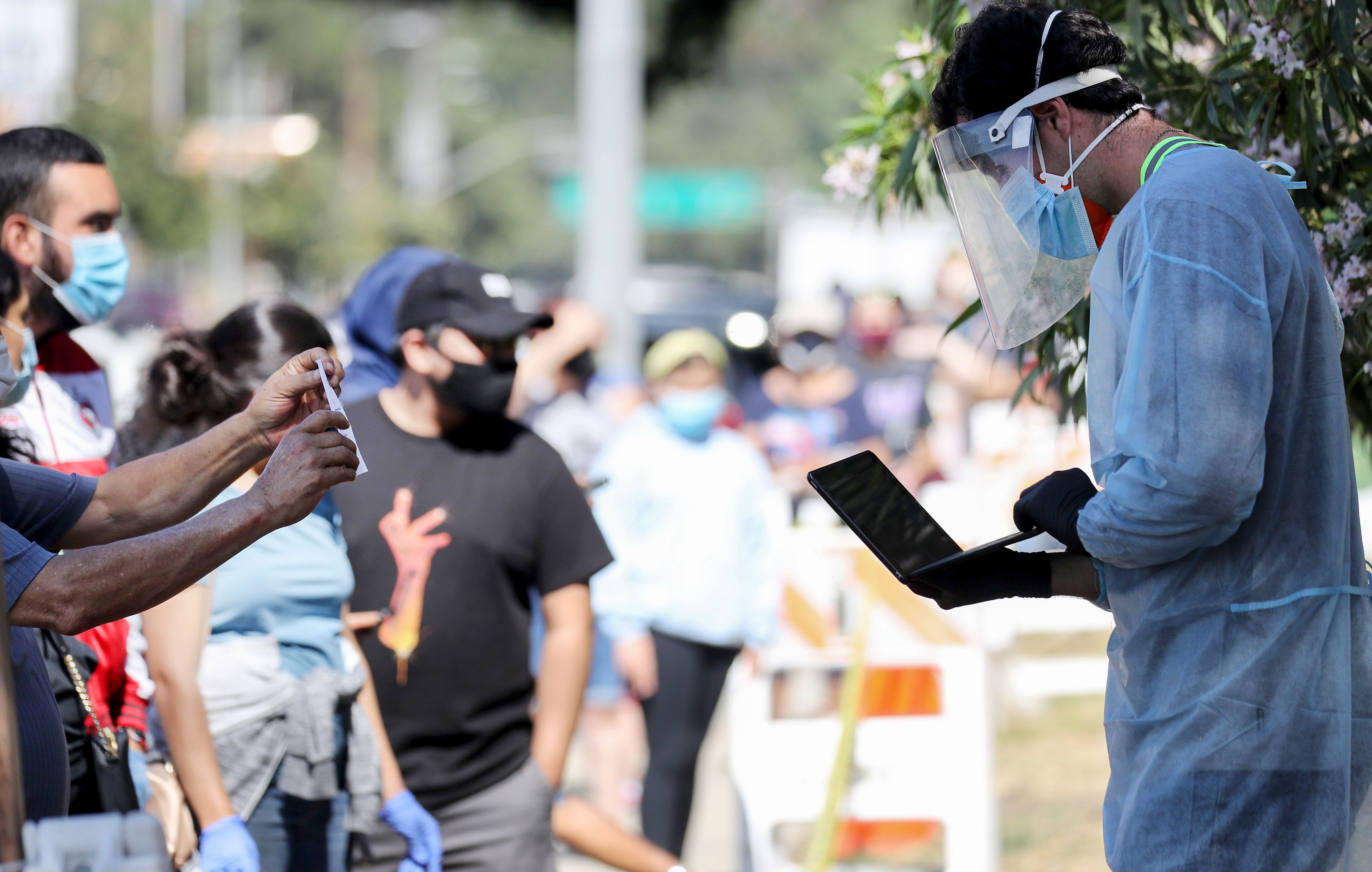 A testing associate dressed in personal protective equipment helps people waiting in line to check in at a COVID-19 testing center at Lincoln Park in Los Angeles on July 7, 2020. (Mario Tama / Getty Images)