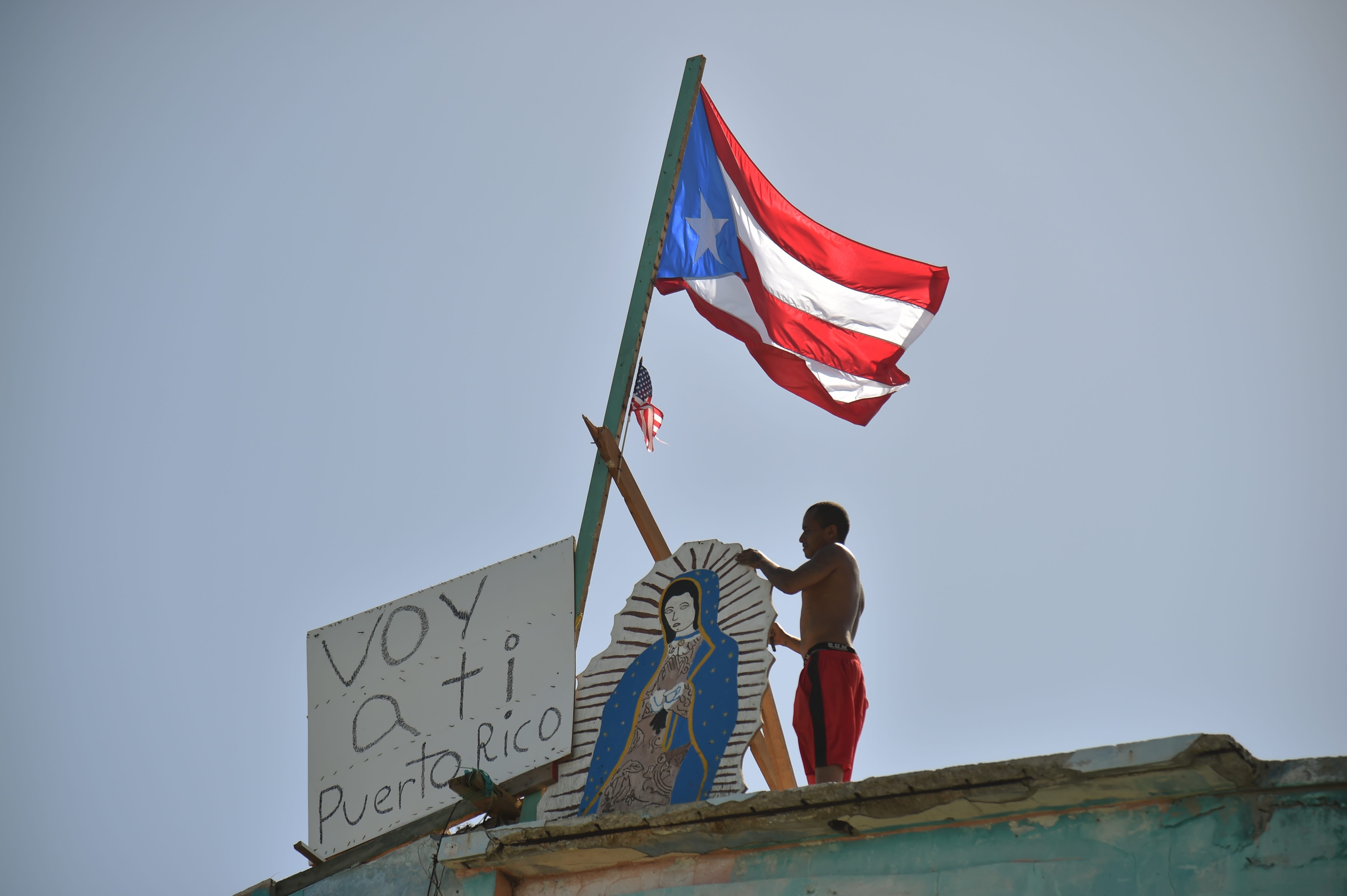 A man places on his house next to a flag of Puerto Rico, a placard that read in Spanish "Voy a ti Puerto Rico" in Yabucoa on Sept. 28, 2017.