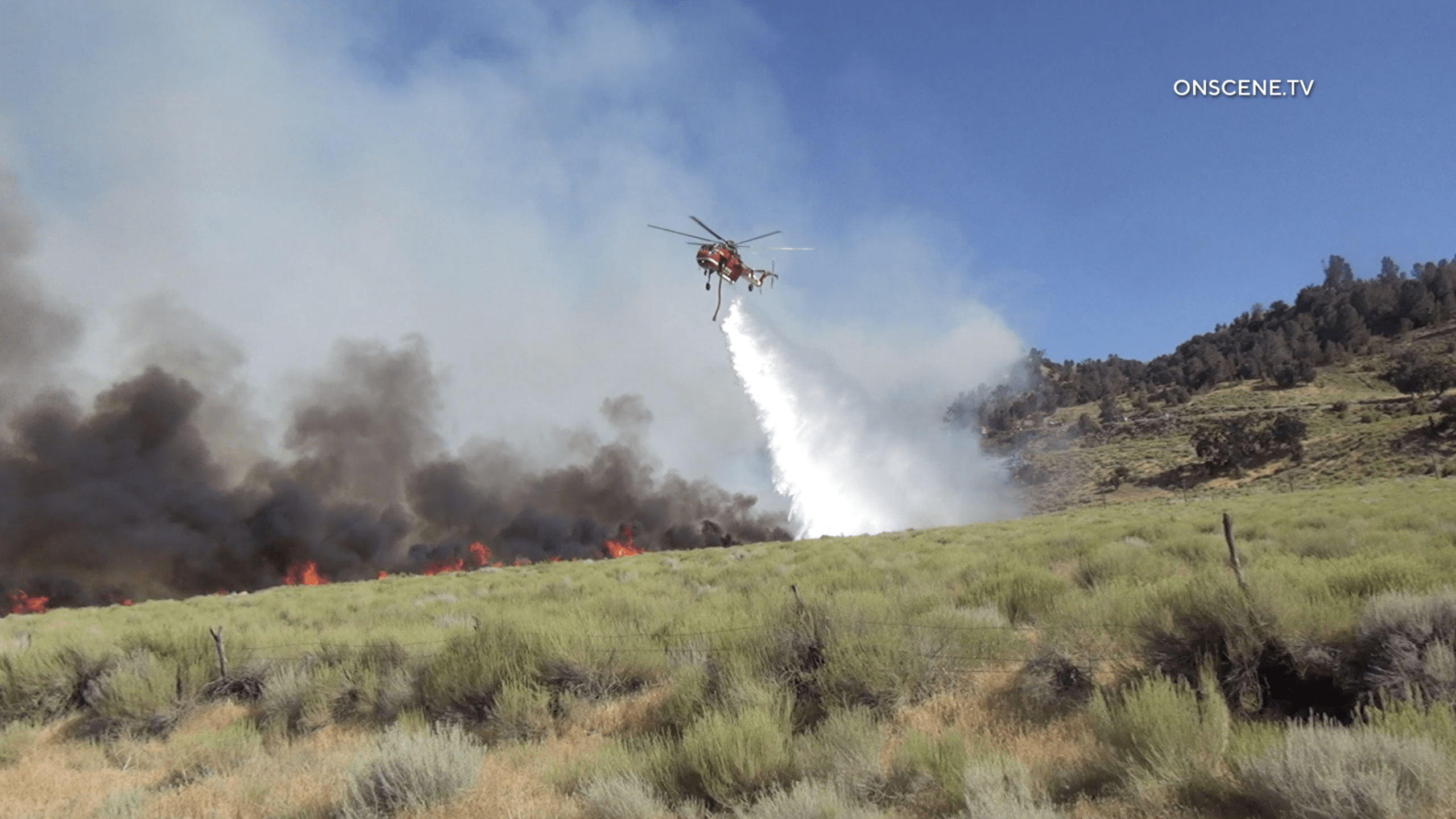 A firefighting helicopter drops water on a brush fire east of the Ridge Route in northern Los Angeles County on July 27, 2020. (OnScene.TV)