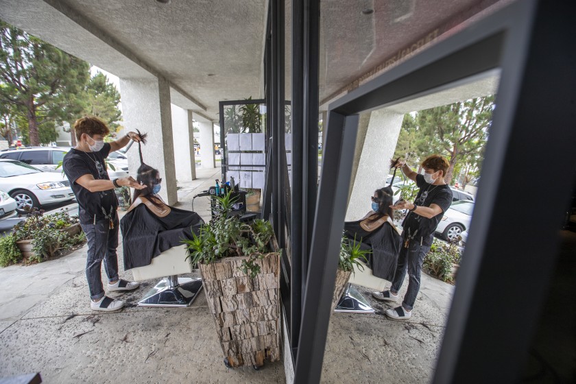 Travis Vu cuts a client’s hair in one of two socially-distanced chairs in front of his salon in Fountain Valley in July 2020. He said he could never have imagined moving his operations outside, but is doing his best to keep business afloat and four employees working. (Allen J. Schaben / Los Angeles Times)