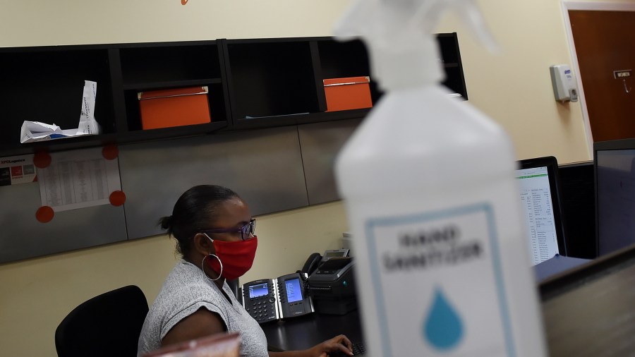 A sanitizer spray bottle is seen on a counter as an employee wearing a face mask works at PastryStar on May 4, 2020, in Laurel, Maryland. (Photo by OLIVIER DOULIERY/AFP via Getty Images)