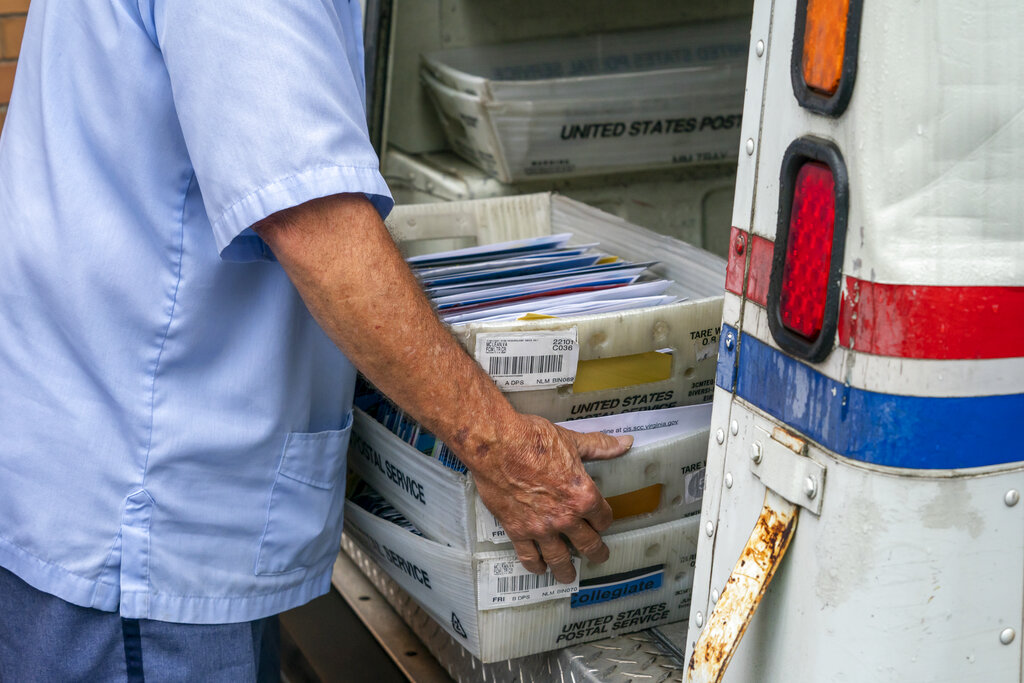 In this July 31, 2020, file photo, letter carriers load mail trucks for deliveries at a U.S. Postal Service facility in McLean, Va. (AP Photo/J. Scott Applewhite, File)