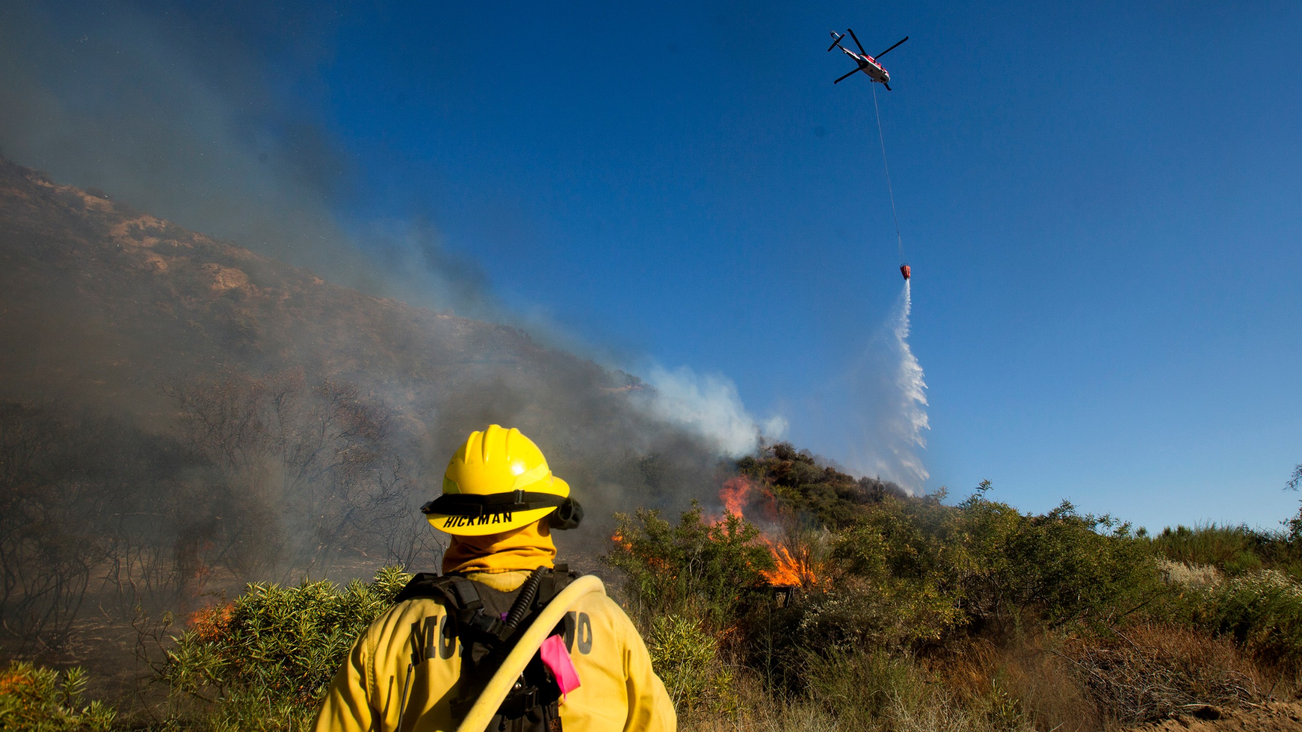 A firefighter watches as a helicopter drops water onto the Apple Fire near Banning, Calif., Sunday, Aug. 2, 2020. (AP Photo/Ringo H.W. Chiu)