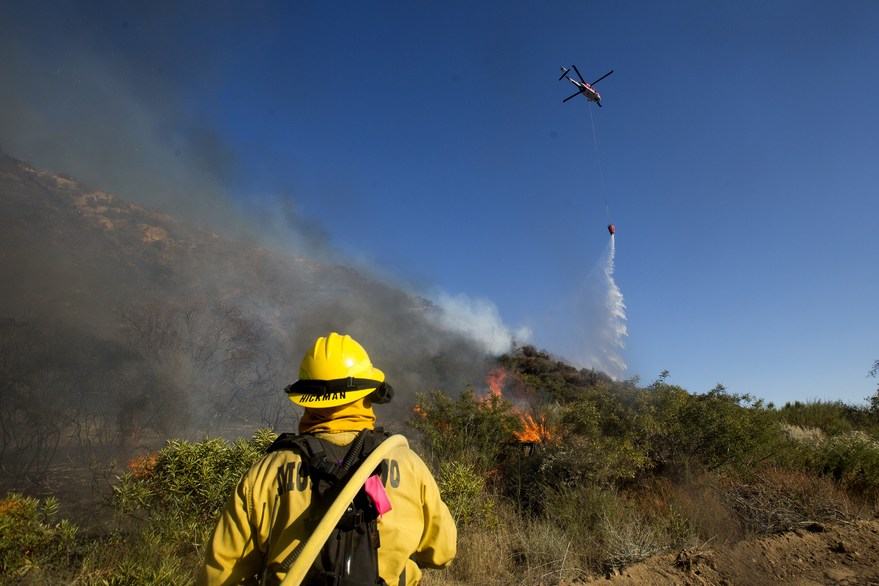 A firefighter watches as a helicopter drops water onto the Apple Fire near Banning, Calif., Sunday, Aug. 2, 2020. (AP Photo/Ringo H.W. Chiu)