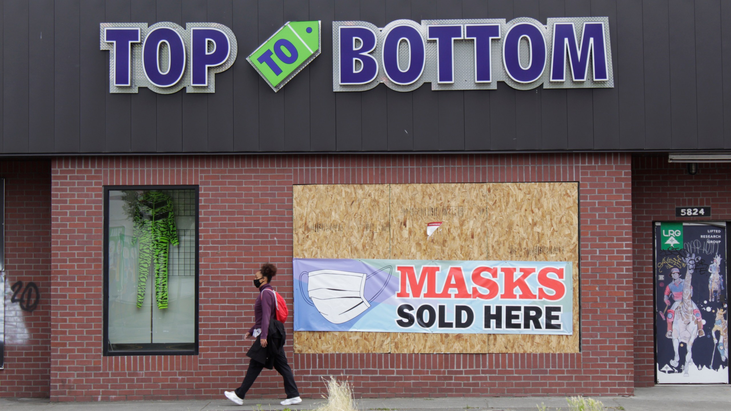 In this July 1, 2020, file photo, a woman walks past a business damaged during recent protests in North Portland, a historically Black neighborhood in Oregon. (AP Photo/Gillian Flaccus, File)