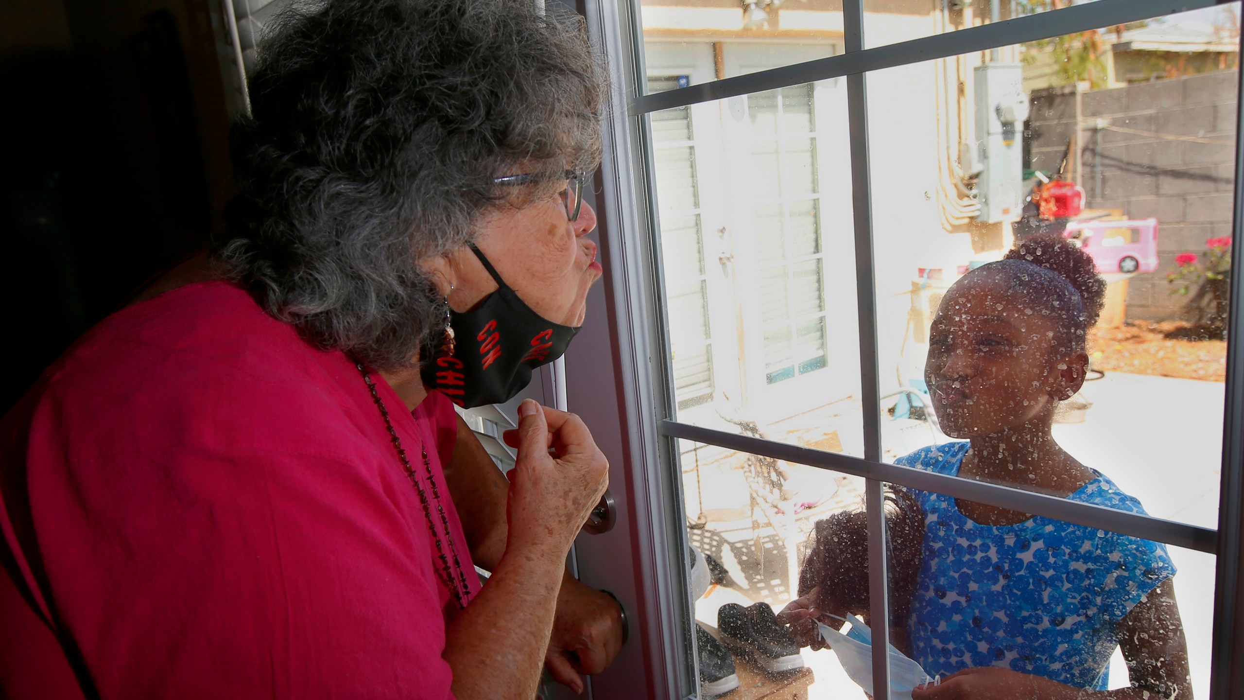 Zita Robinson, left, who's 77 and diabetic, blows a kiss to her granddaughter Traris "Trary" Robinson-Newman, 8, who blows a kiss back to her, Tuesday, Aug. 4, 2020, in Phoenix. (AP Photo/Ross D. Franklin)