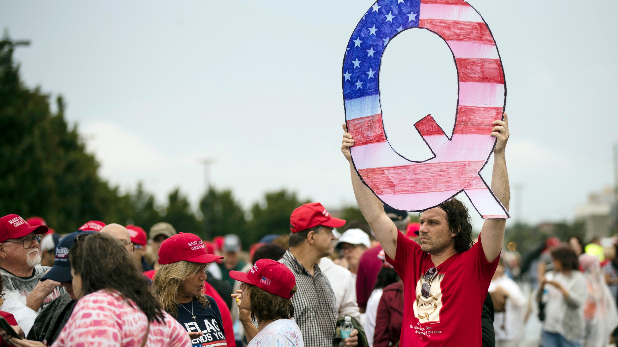 In this Aug. 2, 2018, file photo, a protester holding a Q sign waits in line with others to enter a campaign rally with President Donald Trump in Wilkes-Barre, Pa. (Matt Rourke/Associated Press)