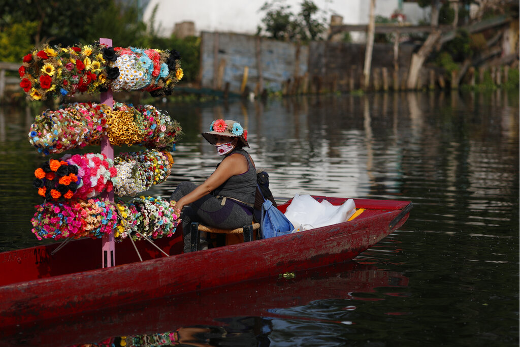 A flower crown vendor waits in her boat for revelers passing in colorfully painted wooden boats known as trajineras at the Nuevo Nativitas dock, as it opens once again to tourists and revelers amidst the ongoing new coronavirus pandemic, the Xochimilco borough of Mexico City, Friday, Aug. 21, 2020. Though traffic was light on the first day back after being closed for several months, gondoliers, handicraft sellers, and food and drink vendors said they were happy to be back at work and to have the chance to earn some money. (AP Photo/Rebecca Blackwell)