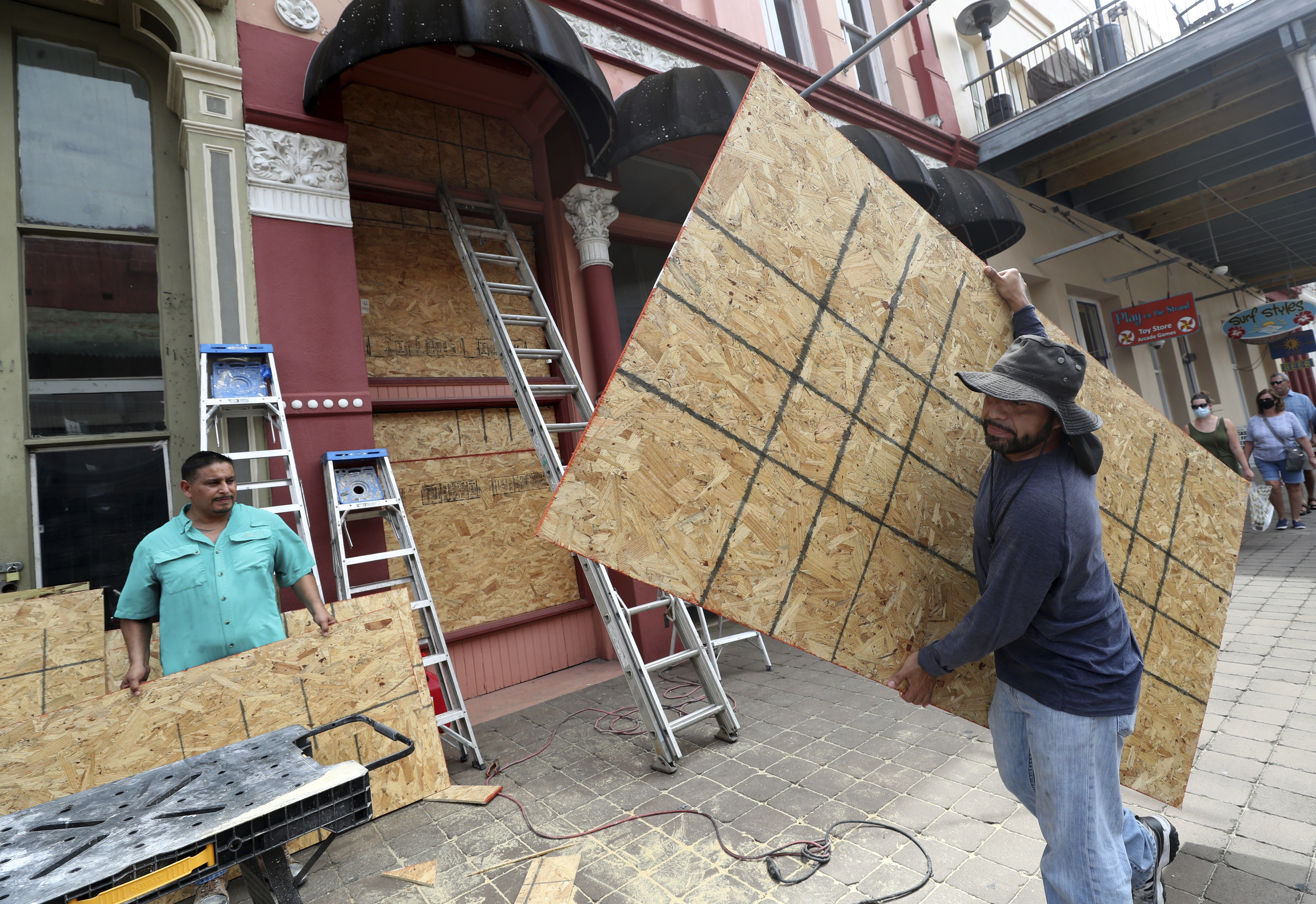 Cesar Reyes, right, carries a sheet of plywood to cut to size as he and Robert Aparicio, left, and Manuel Sepulveda, not pictured, install window coverings at Strand Brass and Christmas on the Strand, 2115 Strand St., in Galveston on Monday, Aug. 24, 2020. ( Jennifer Reynolds/The Galveston County Daily News via AP)