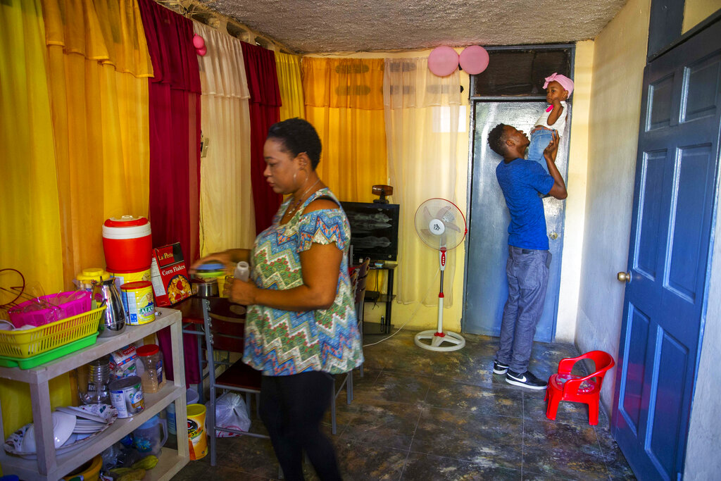 Verty plays with his 1-year-old daughter while his wife Saint Jean fixes the house in Port-au-Prince, Haiti, Tuesday, Aug. 25, 2020. (AP Photo/Dieu Nalio Chery)