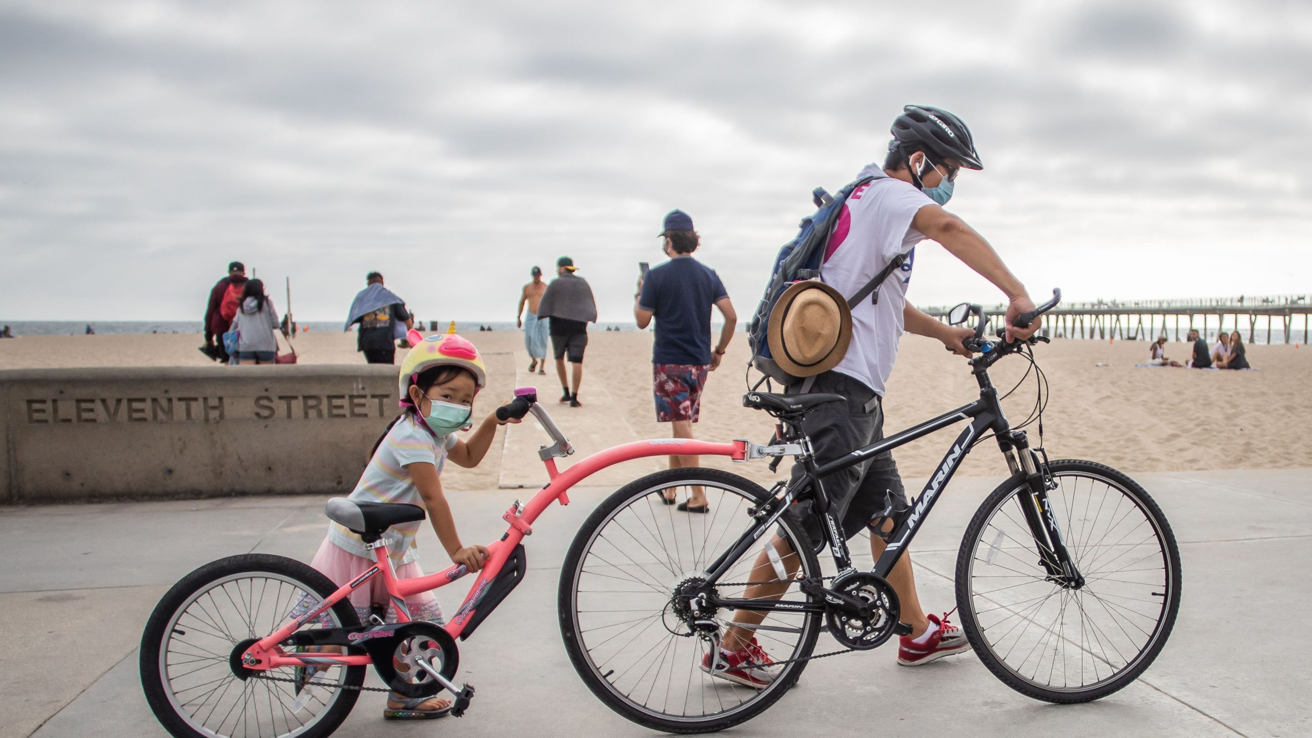 A girl and her father wear facemasks while they push their bikes in Hermosa Beach on July 14, 2020. (Apu GOMES / AFP via Getty Images)