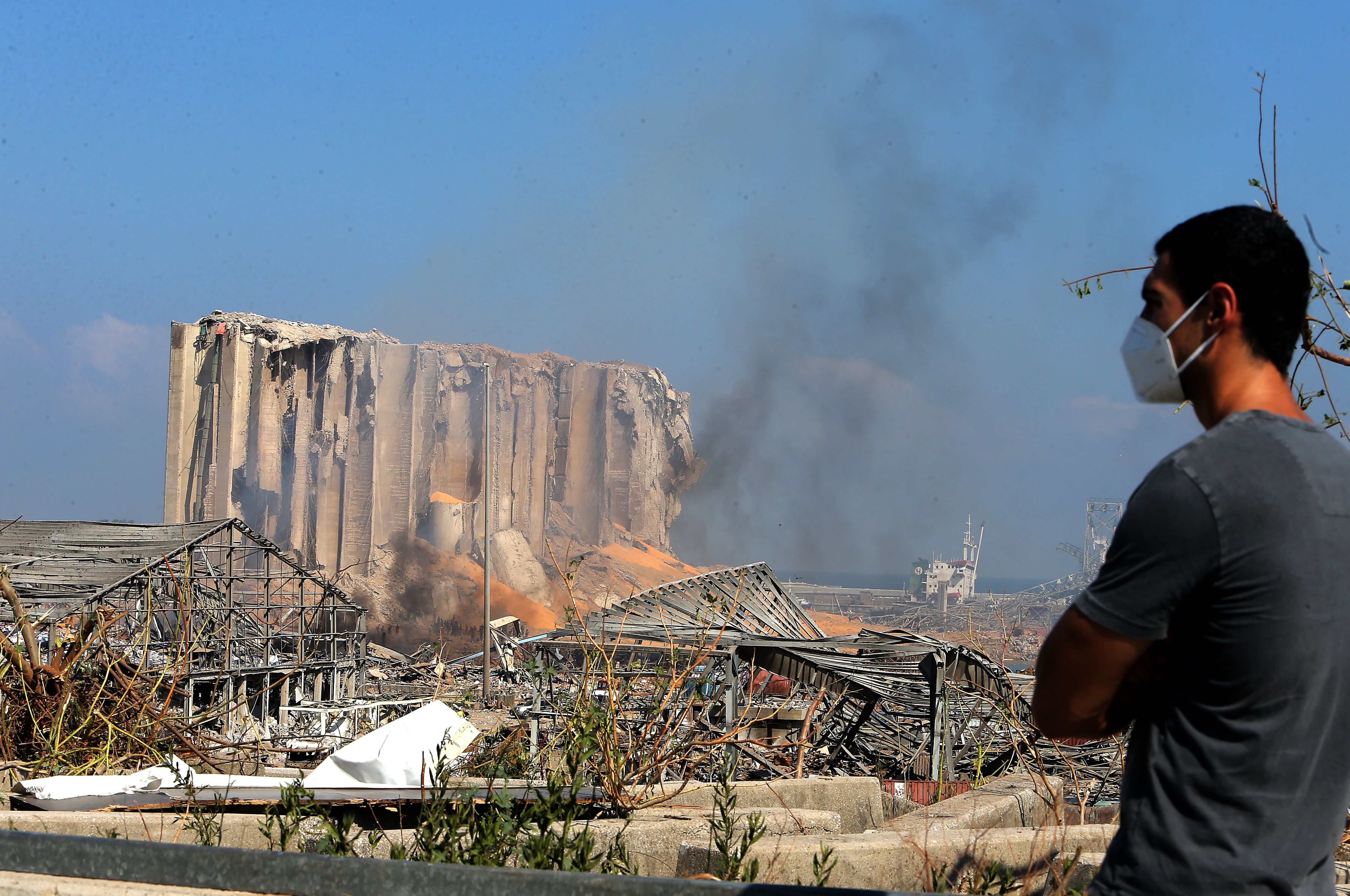 A man wearing a protective mask against the coronavirus stands across the road from the damaged grain silos of Beirut's harbour August 5, 2020, one day after a powerful twin explosion tore through Lebanon's capital, resulting from the ignition of a huge depot of ammonium nitrate at the city's main port. (STR/AFP via Getty Images)