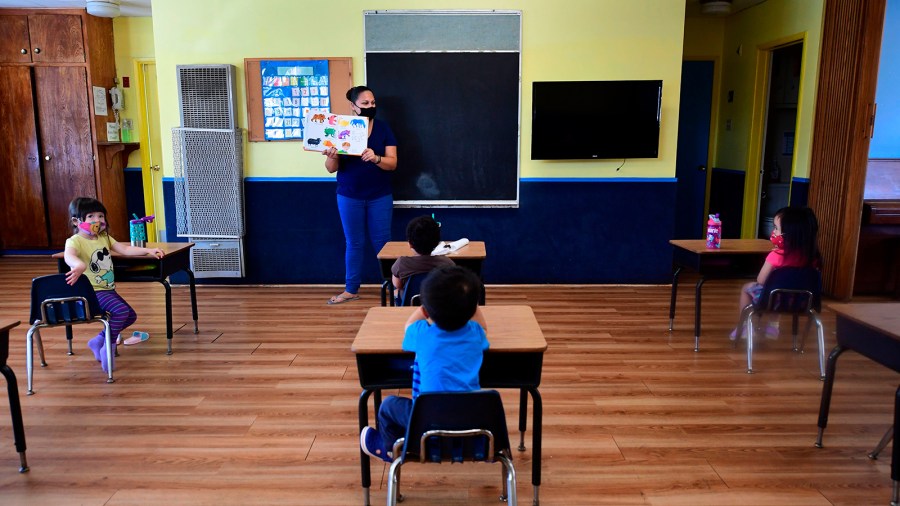 An instructor reads to children in a pre-school class, wearing masks and at desks spaced apart as per coronavirus guidelines during summer school sessions at Happy Day School in Monterey Park, California on July 9, 2020. (FREDERIC J. BROWN/AFP via Getty Images)