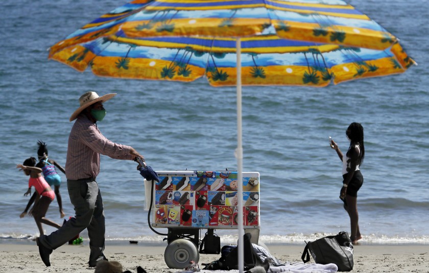 An ice cream vendors pushes a cart along the sand at Junipero Beach in Long Beach on a warm afternoon in 2020. (Luis Sinco / Los Angeles Times)