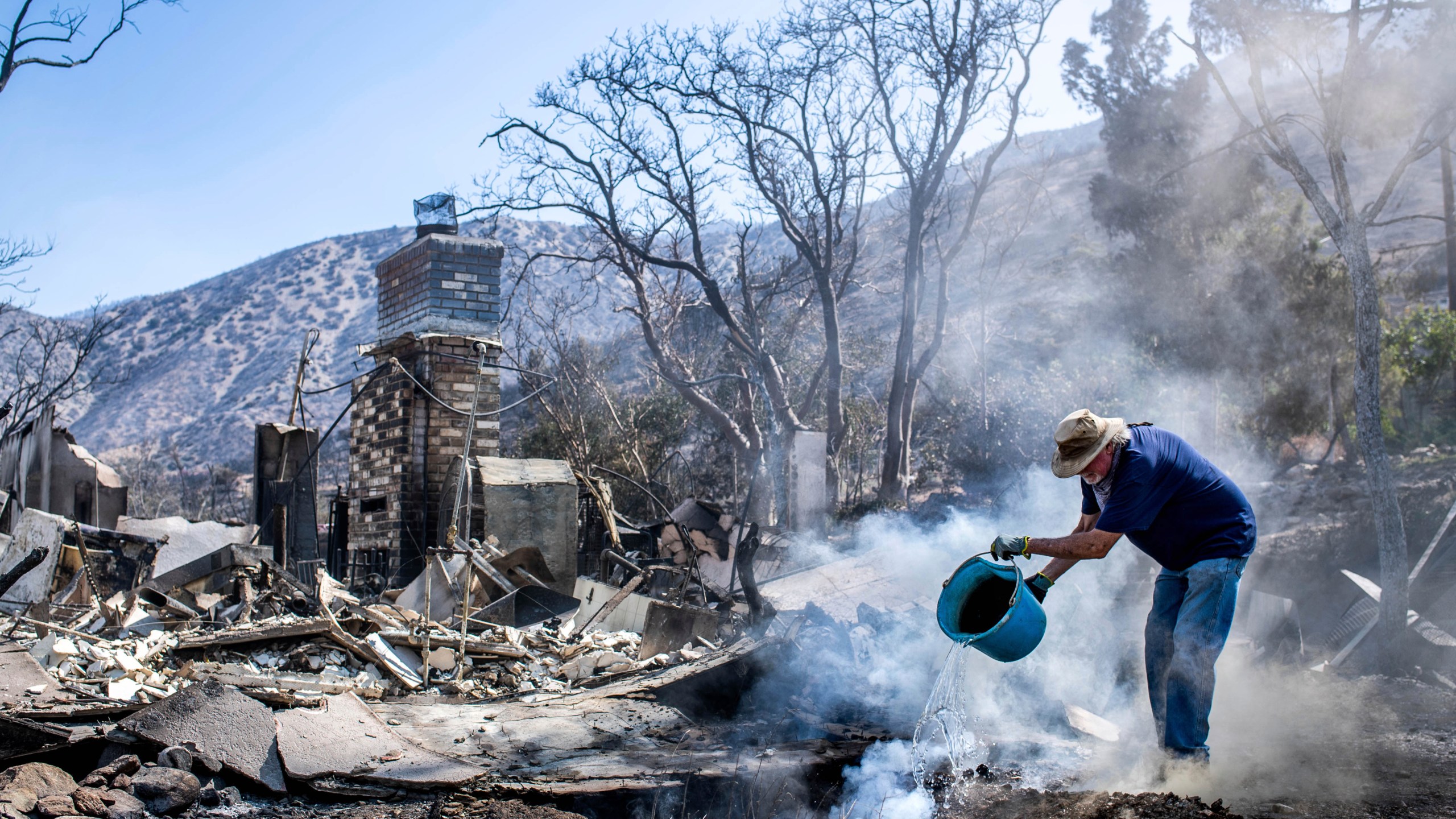 Dale Burton, of Leona Valley, tries to put out the fire that continues to smolder at his friend Cheryl Poindexter's property on Monday, Sept. 21, 2020, after the Bobcat Fire burned her home of 27 years and the 11-acre property where she ran an animal rescue in Juniper Hills. (Sarah Reingewirtz/The Orange County Register via AP)