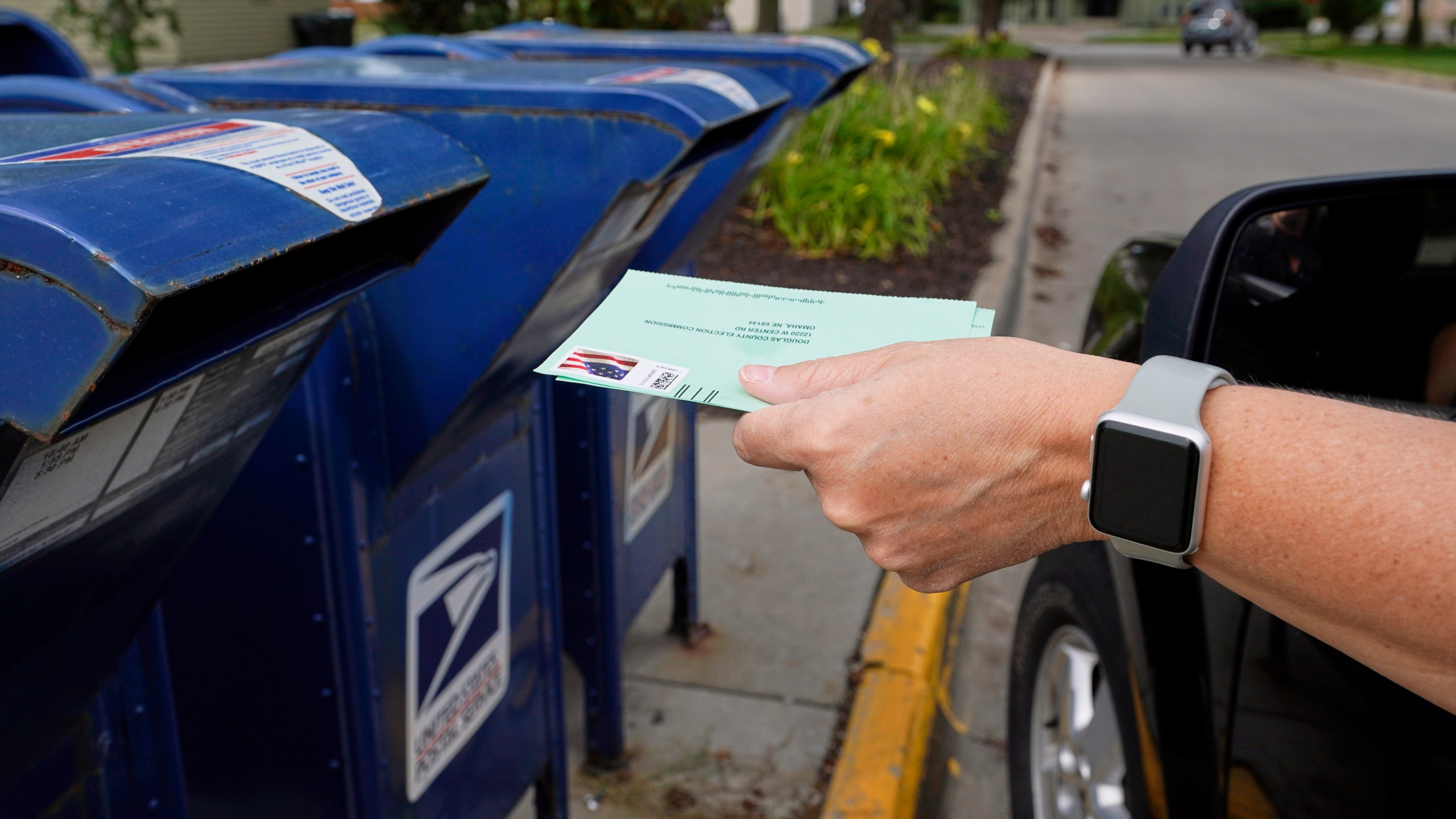 In this Tuesday, Aug. 18, 2020, file photo, a person drops applications for mail-in-ballots into a mailbox in Omaha, Neb. Data obtained by The Associated Press shows Postal Service districts across the nation are missing the agency’s own standards for on-time delivery as millions of Americans prepare to vote by mail. (AP Photo/Nati Harnik, File)